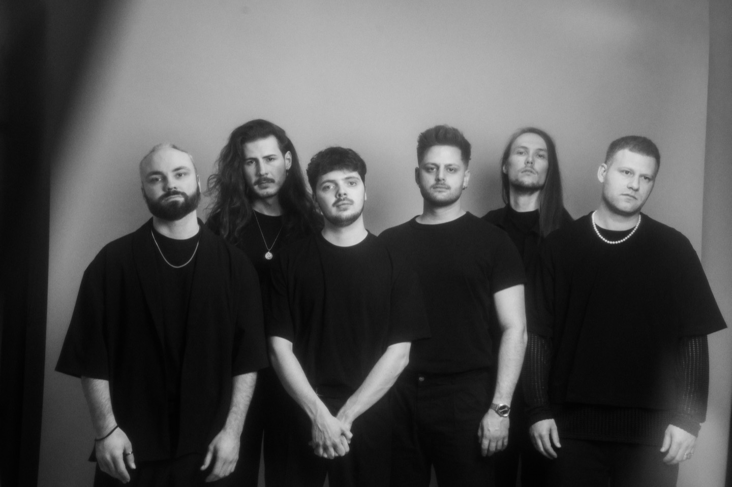 The six members of One Lunar Day lined up against a pale studio wall, all dressed in black.