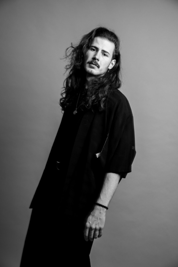 Dave of One Lunar Day, photographed in black against a pale studio wall.